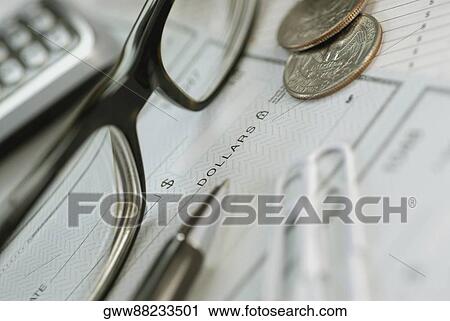 Stock Image - Close-up of a pair of eyeglasses with coins and a pen on a check. Fotosearch
