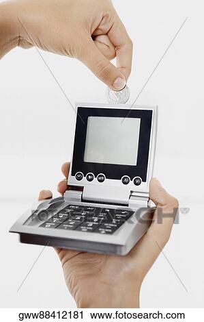 Stock Image - Close-up of a person's hand inserting a coin into a calculator. Fotosearch