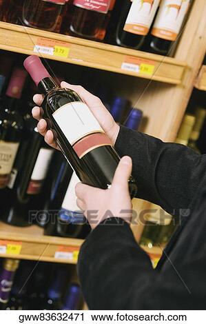 Stock Image - Close-up of a person's hands holding a wine bottle in a liquor store. Fotosearch