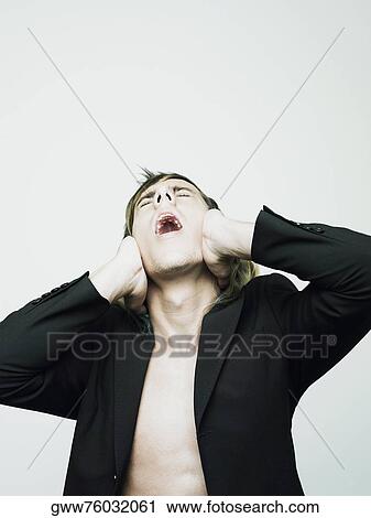 Stock Image - Close-up of a young man covering his ears with his hands and screaming. Fotosearch