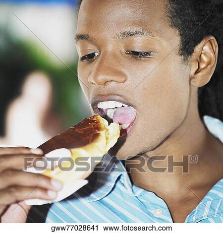 Stock Image - Close-up of a young man eating a pastry. Fotosearch