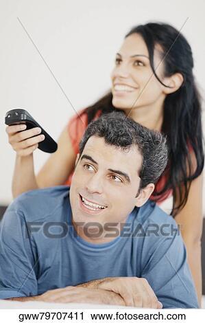 Close-up of a young woman and a mid adult man watching television and smiling View Large Photo Image Stock Image - Close-up of a young woman and a mid adult man watching television and smiling. Fotosearch