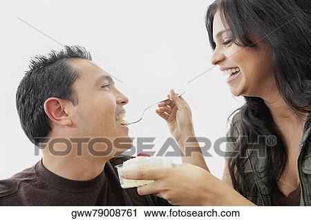 Stock Image - Close-up of a young woman feeding a mid adult man. Fotosearch
