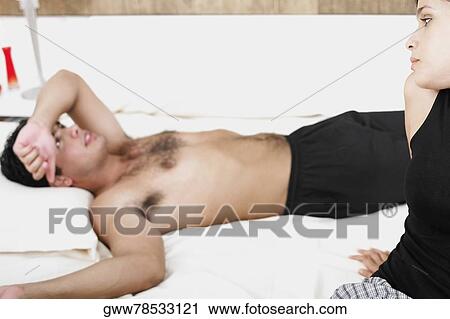 Stock Image - Close-up of a young woman looking at a young man lying on the bed. Fotosearch
