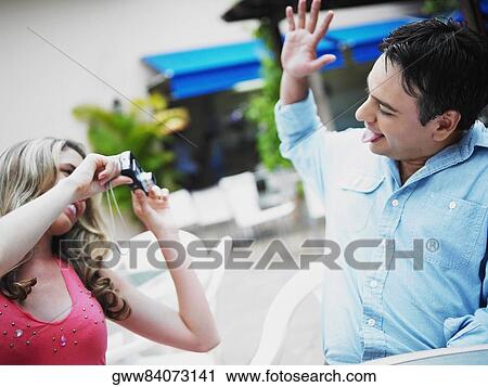 Stock Image - Close-up of a young woman taking a picture of a young man. Fotosearch