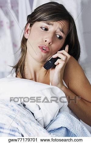 Stock Image - Close-up of a young woman talking on the phone and carrying clothes. Fotosearch