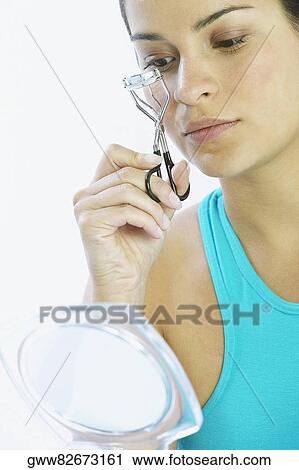 Stock Image - Close-up of a young woman using an eyelash curler. Fotosearch