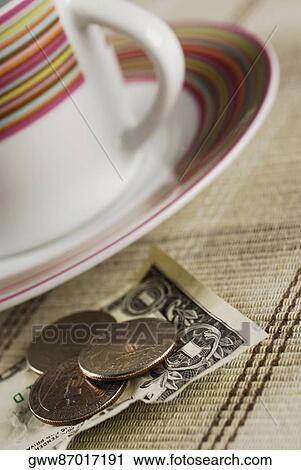 Stock Image - Close-up of coins on an American one dollar note beside a tea cup. Fotosearch
