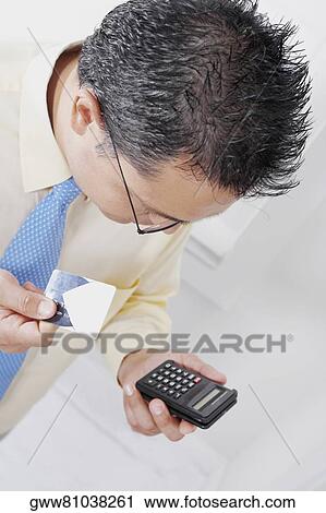 Stock Image - High angle view of a businessman holding a calculator and a credit card. Fotosearch