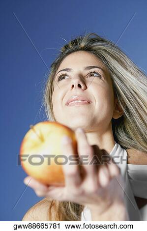 Stock Image - Low angle view of a mid adult woman holding an apple. Fotosearch