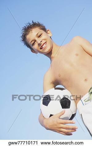 Stock Image - Low angle view of a teenage boy holding a soccer ball. Fotosearch