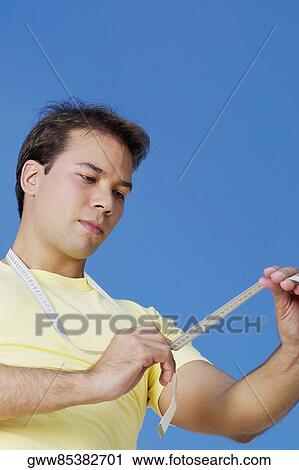 Low angle view of a young man holding a tape measure around his neck View Large Photo Image Stock Image - Low angle view of a young man holding a tape measure around his neck. Fotosearch