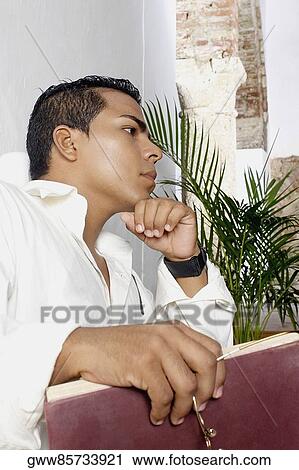 Low angle view of a young man holding a book and looking away View Large Photo Image Stock Image - Low angle view of a young man holding a book and looking away. Fotosearch