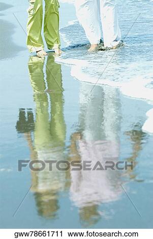 Stock Image - Low section view of two people standing on the beach. Fotosearch