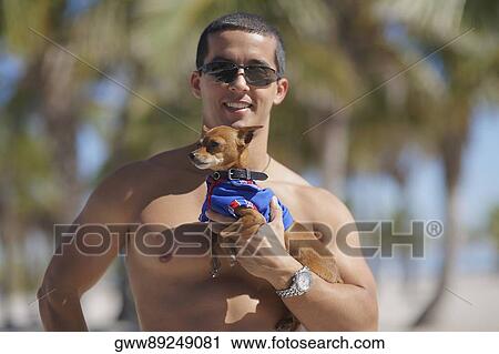 Stock Image - Mid adult man holding a dog and smiling. Fotosearch