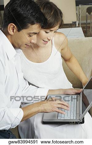 Stock Image - Mid adult man using a laptop with a young woman beside him. Fotosearch