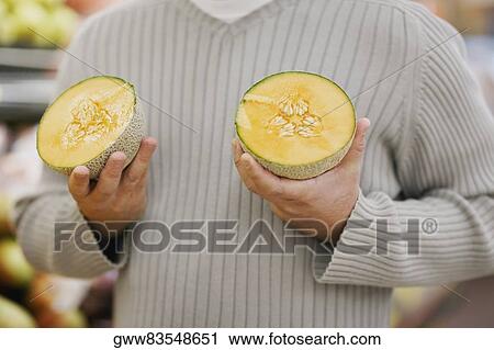 Stock Image - Mid section view of a man holding melon slices. Fotosearch