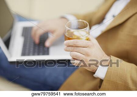 Mid section view of a man using a laptop and holding a glass of wine View Large Photo Image Stock Image - Mid section view of a man using a laptop and holding a glass of wine. Fotosearch