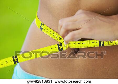 Mid section view of a woman measuring her waist with a tape measure View Large Photo Image Stock Image - Mid section view of a woman measuring her waist with a tape measure. Fotosearch
