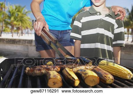 Mid section view of a young woman and her son grilling banana and corn View Large Photo Image Stock Image - Mid section view of a young woman and her son grilling banana and corn. Fotosearch