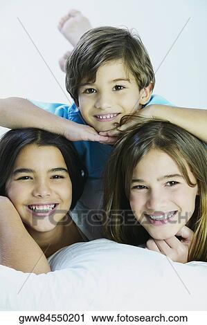 Stock Image - Portrait of a boy lying on the bed with his sisters. Fotosearch