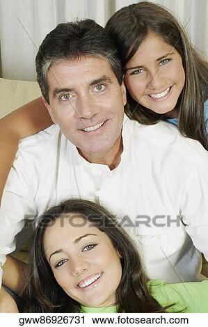 Portrait of a mature man and his two daughters sitting on a couch and smiling View Large Photo Image Stock Image - Portrait of a mature man and his two daughters sitting on a couch and smiling. Fotosearch