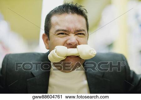 Stock Image - Portrait of a mid adult man with a dog bone in his mouth. Fotosearch