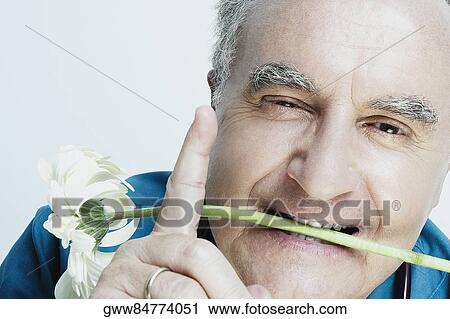 Stock Image - Portrait of a senior man holding a flower in his mouth and pointing. Fotosearch