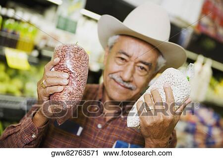 Stock Image - Portrait of a senior man holding two packets of grain. Fotosearch