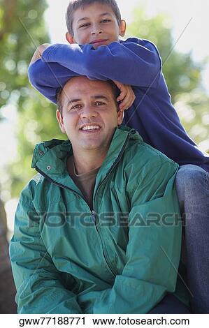 Stock Image - Portrait of a teenage boy leaning over his father. Fotosearch