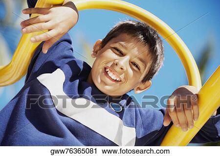 Stock Image - Portrait of a teenage boy smiling on a jungle gym. Fotosearch