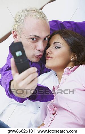 Portrait of a young couple taking a photograph of themselves with a mobile phone View Large Photo Image Stock Image - Portrait of a young couple taking a photograph of themselves with a mobile phone. Fotosearch