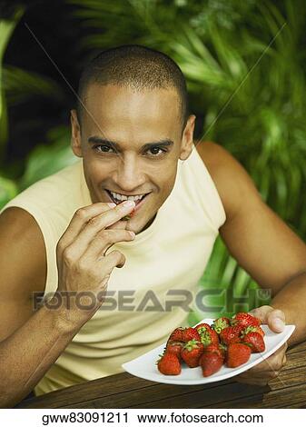 Stock Image - Portrait of a young man eating a strawberry. Fotosearch