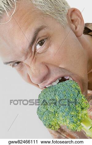 Stock Image - Portrait of a young man eating broccoli. Fotosearch