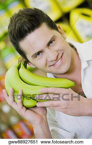 Portrait of a young man holding a bunch of bananas in a supermarket View Large Photo Image Stock Image - Portrait of a young man holding a bunch of bananas in a supermarket. Fotosearch