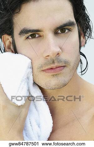 Stock Image - Portrait of a young man wiping his face with a towel. Fotosearch