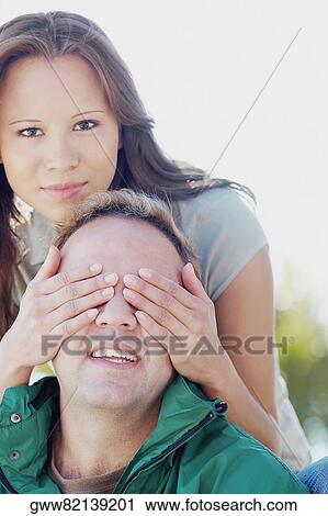 Portrait of a young woman covering a mid adult man's eyes View Large Photo Image Stock Image - Portrait of a young woman covering a mid adult man's eyes. Fotosearch