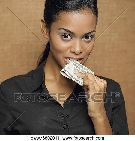Stock Image - Portrait of a young woman holding a paper currency in her mouth. Fotosearch