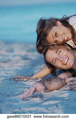 Portrait of a young woman lying on top of a mid adult man on the beach View Large Photo Image Stock Image - Portrait of a young woman lying on top of a mid adult man on the beach. Fotosearch