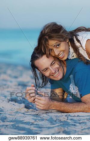 Portrait of a young woman lying on top of a mid adult man on the beach View Large Photo Image Stock Image - Portrait of a young woman lying on top of a mid adult man on the beach. Fotosearch