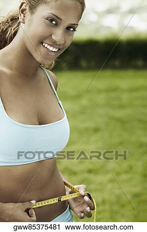 Portrait of a young woman measuring her waist with a tape measure View Large Photo Image Stock Image - Portrait of a young woman measuring her waist with a tape measure. Fotosearch