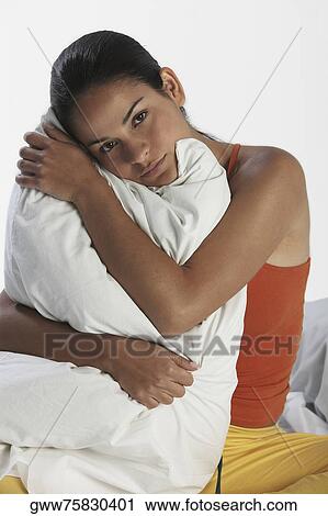 Portrait of a young woman sitting on the bed and hugging a pillow View Large Photo Image Stock Image - Portrait of a young woman sitting on the bed and hugging a pillow. Fotosearch