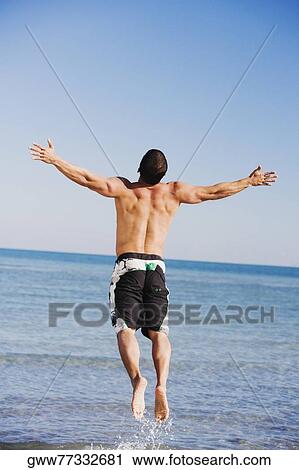 Rear view of a mid adult man with his arms outstretched jumping on the beach View Large Photo Image Stock Image - Rear view of a mid adult man with his arms outstretched jumping on the beach. Fotosearch