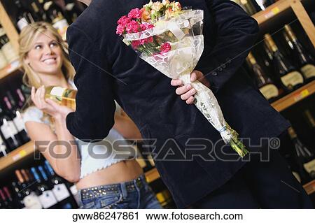 Rear view of a young man hiding bouquet of flowers behind his back from a young woman View Large Photo Image Stock Image - Rear view of a young man hiding bouquet of flowers behind his back from a young woman. Fotosearch
