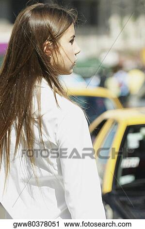 Stock Image - Rear view of a young woman standing at the roadside. Fotosearch