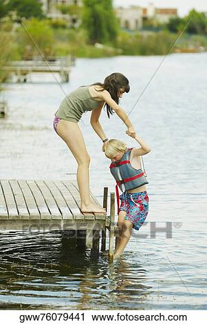 Side profile of a girl standing on a pier and helping her brother out of a lake View Large Photo Image Stock Image - Side profile of a girl standing on a pier and helping her brother out of a lake. Fotosearch