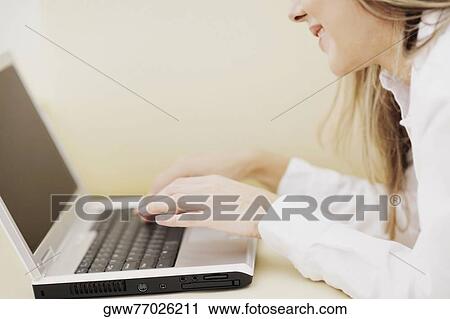 Stock Image - Side profile of a mid adult woman using a laptop and smiling. Fotosearch