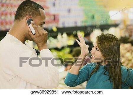Stock Image - Side profile of a young man talking on a mobile phone and a young woman looking at him. Fotosearch