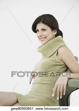 Stock Image - Side profile of a young woman sitting on a chair and smiling. Fotosearch