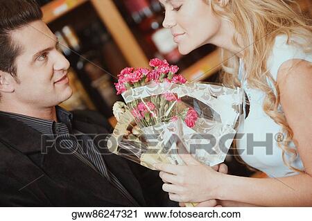 Side profile of a young woman smelling a bouquet of flowers in front of a young man View Large Photo Image Stock Image - Side profile of a young woman smelling a bouquet of flowers in front of a young man. Fotosearch